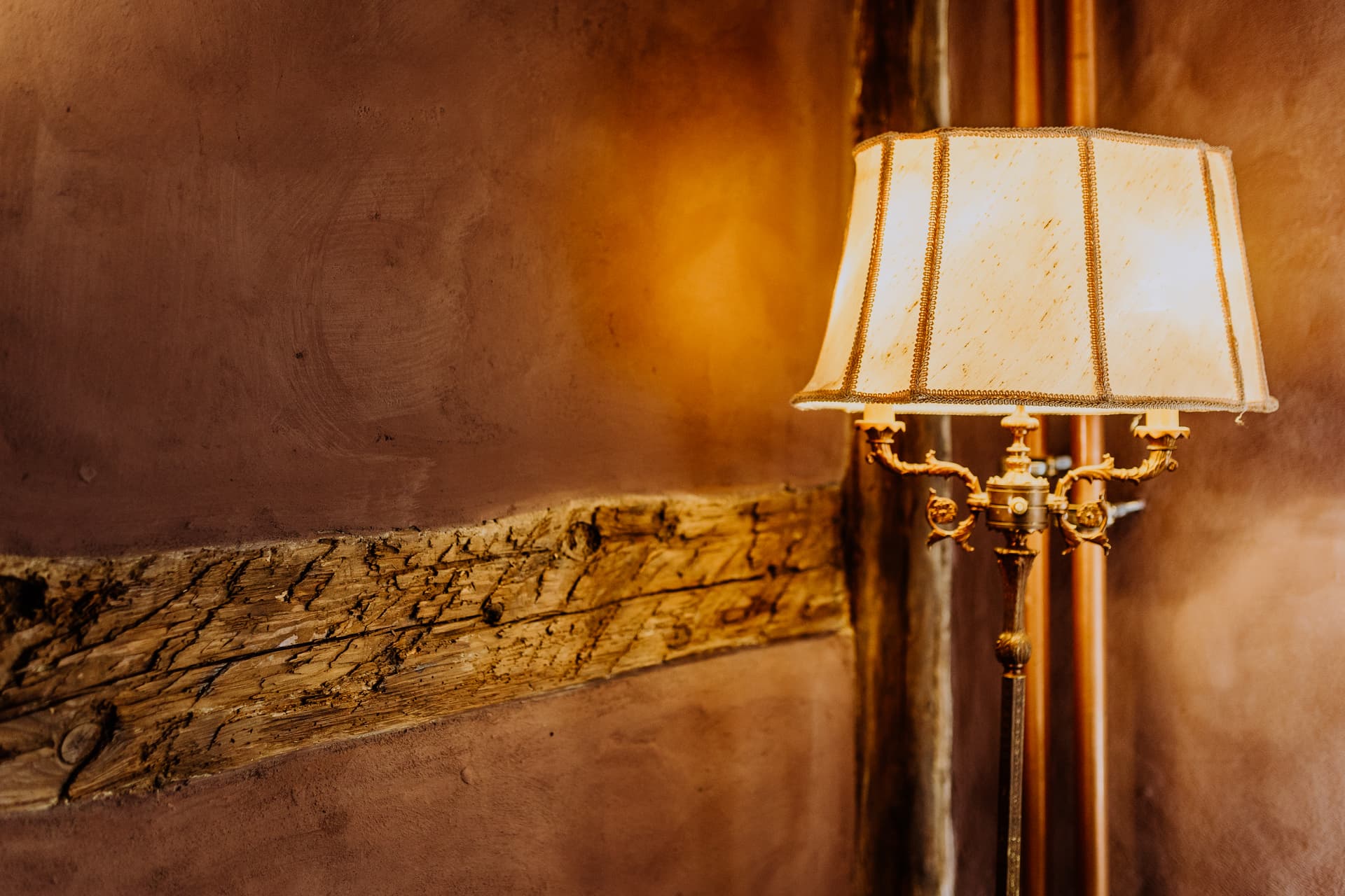Warme Lichtstimmung im Badezimmer mit verzierter Messing-Stehleuchte und historischen Deckenbalken