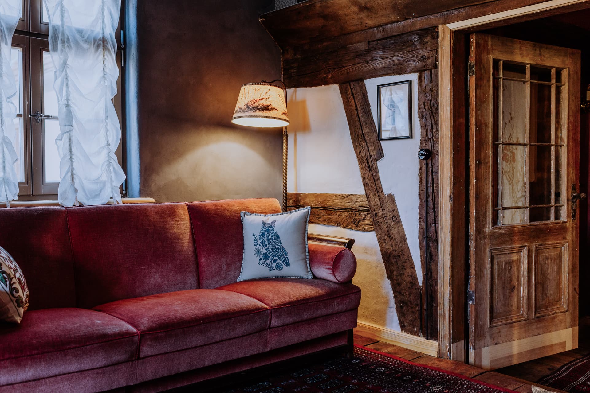 Leseecke mit weinrotem Samtsofa, Eulen-Stickkissen, Stehlampe und freigelegtem Fachwerkbalken