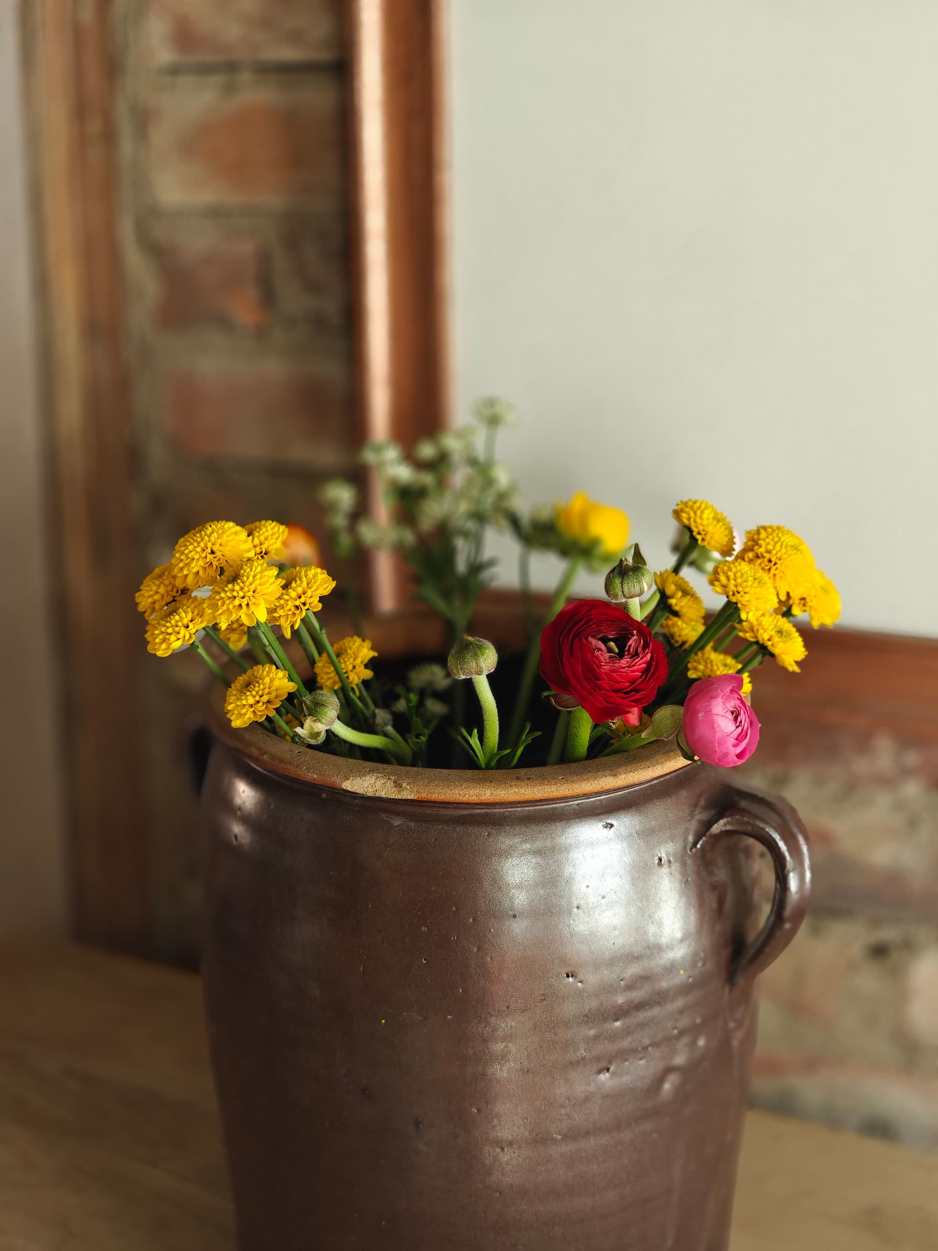 Frischer Frühlingsstrauß mit gelben Chrysanthemen und bunten Ranunkeln im braunen Tonkrug