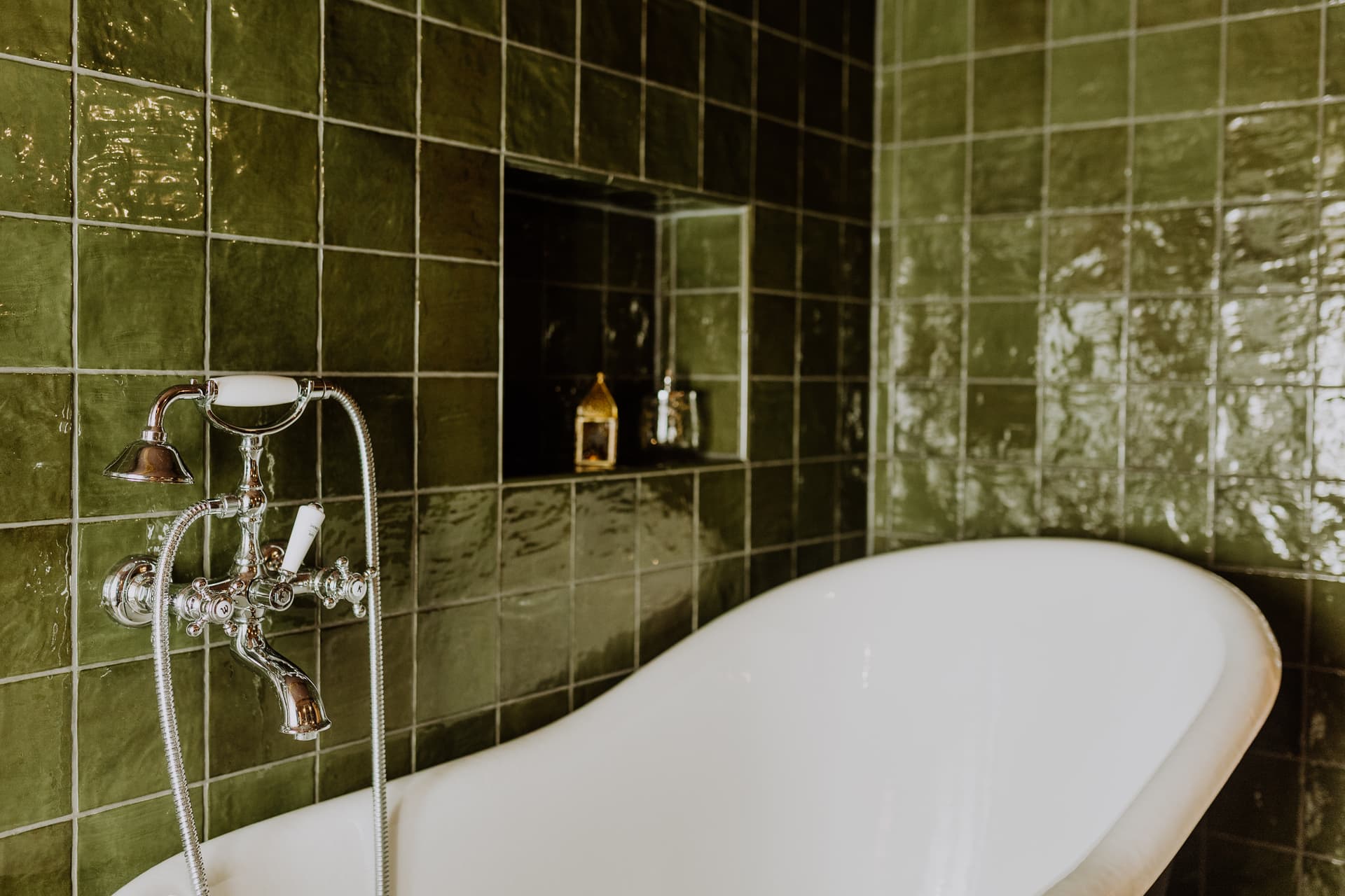Freistehende weiße Badewanne mit verchromter Telefondusche vor glänzenden waldgrünen Fliesen